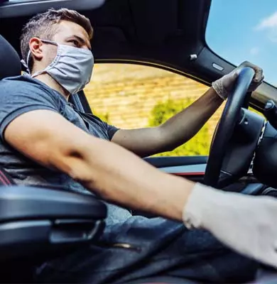 Ein Autofahrer fährt mit Schutzmaske und Handschuhen